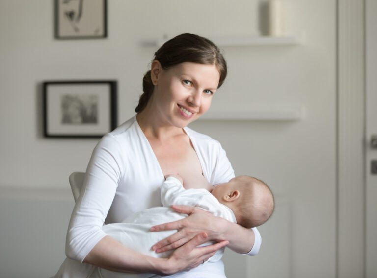 Portrait of a young smiling attractive woman breastfeeding a child, holding on her hands, sitting, looking at the camera. New born, bonding concept photo